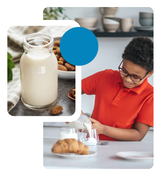 Botella de leche de almendras rodeada de almendras y tela, junto a una persona sirviendo leche en un vaso con un croissant y vajilla sobre la mesa. Fondo con estantería de cocina.